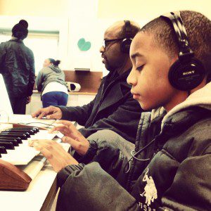A young person with headphones plays a keyboard. A teaching artist appears in the background.
