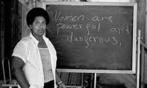 Audre Lorde stands next to a blackboard with these words written on it: 