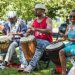 Three Black people playing the drums in a park.
