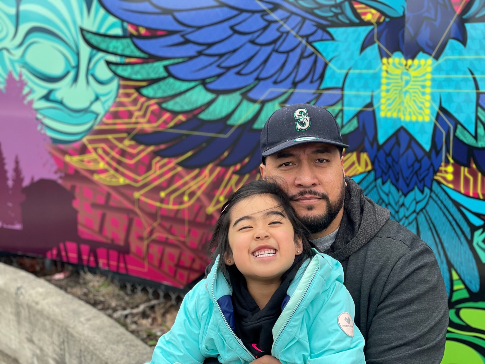 Artist Toka Valu with his daughter in front of a colorful mural