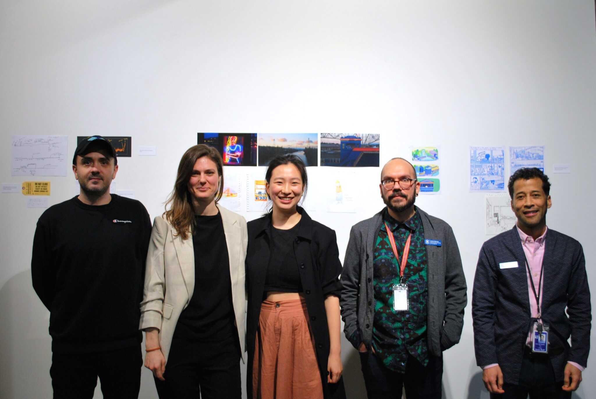 Group photo of five people standing in a line in front of art on a gallery wall
