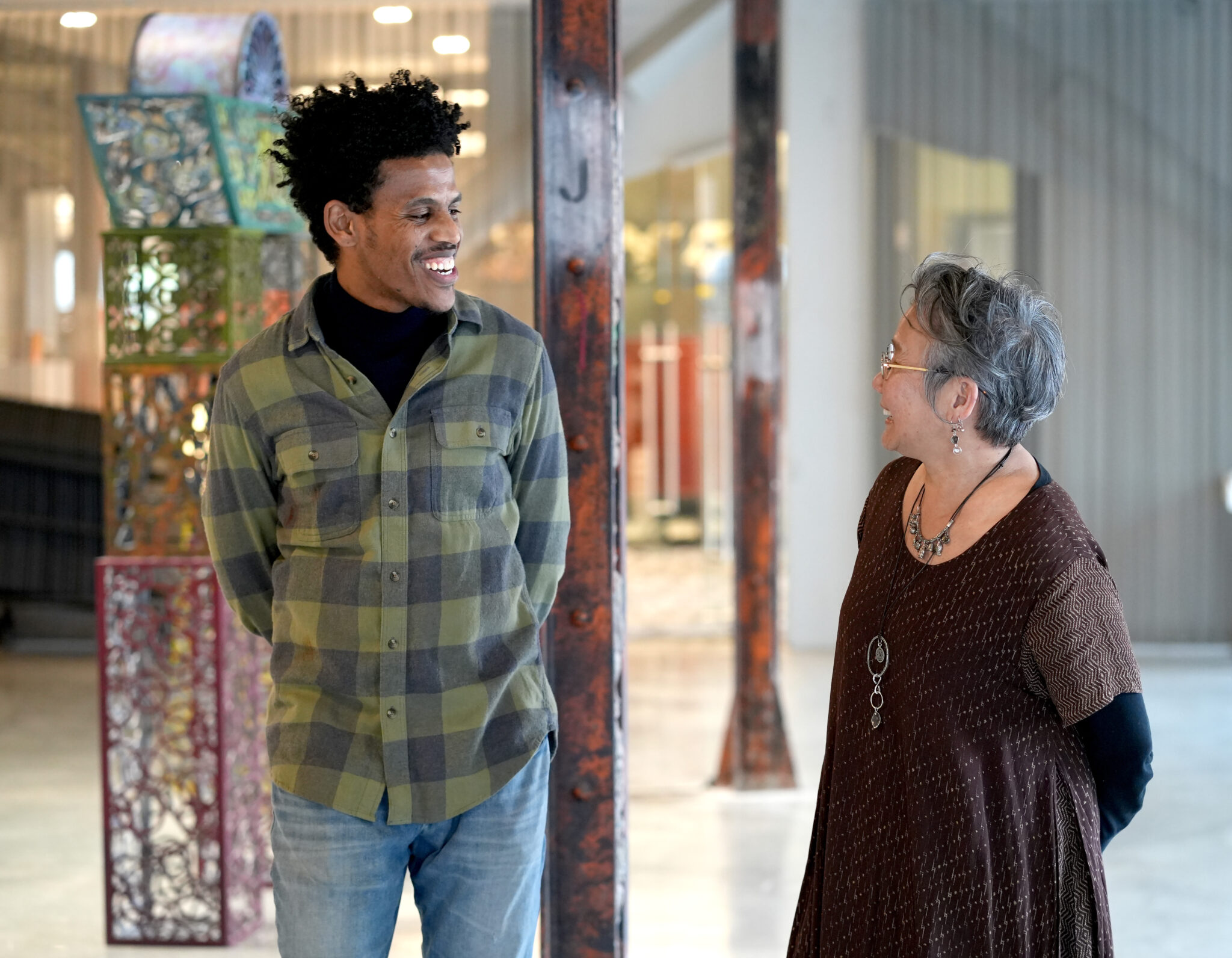Artists Nahom Ghirmay and June Sekiguchi smiling at each other in the gallery