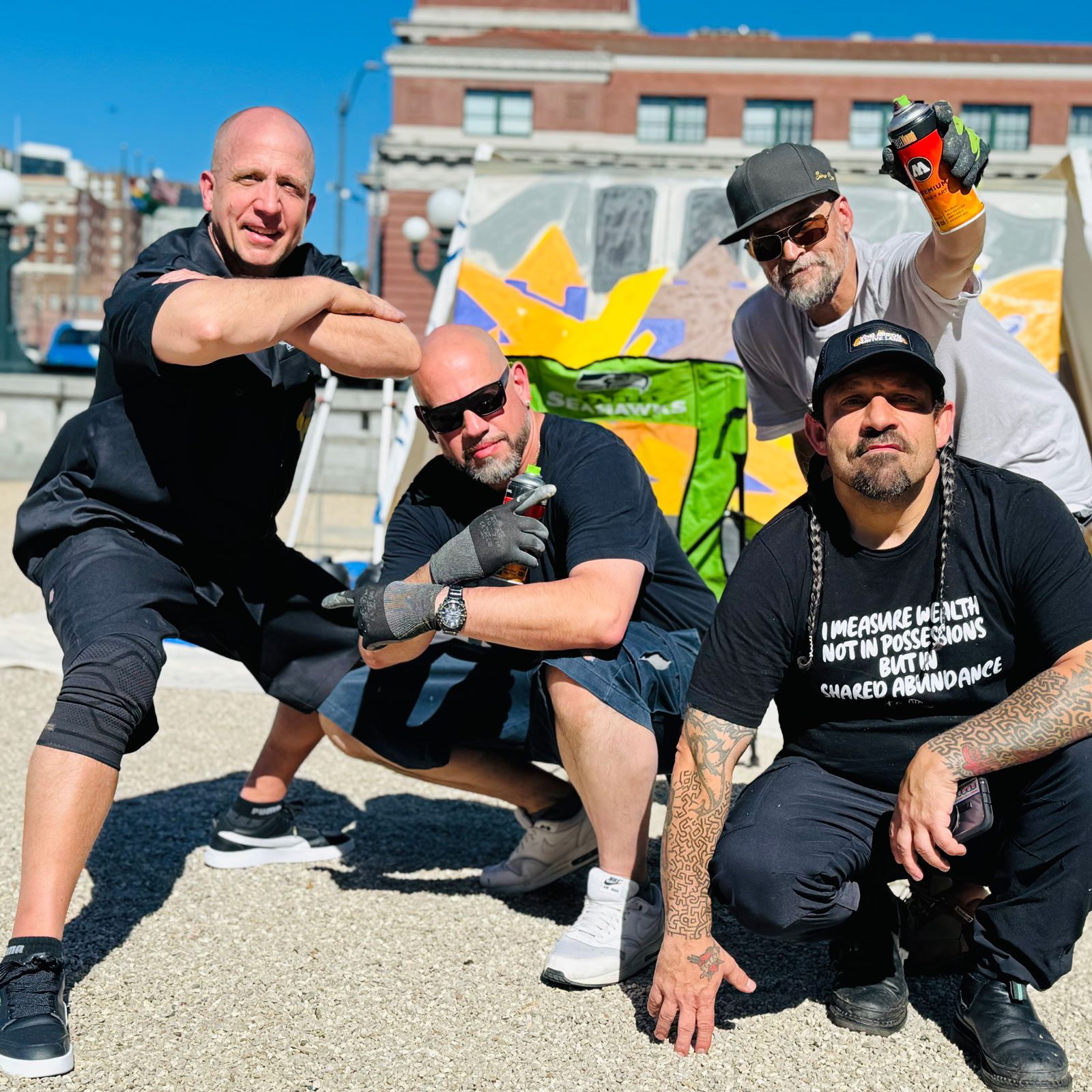 Three graffiti writers strike poses, two holding spray cans. A fourth member of their crew joins them.