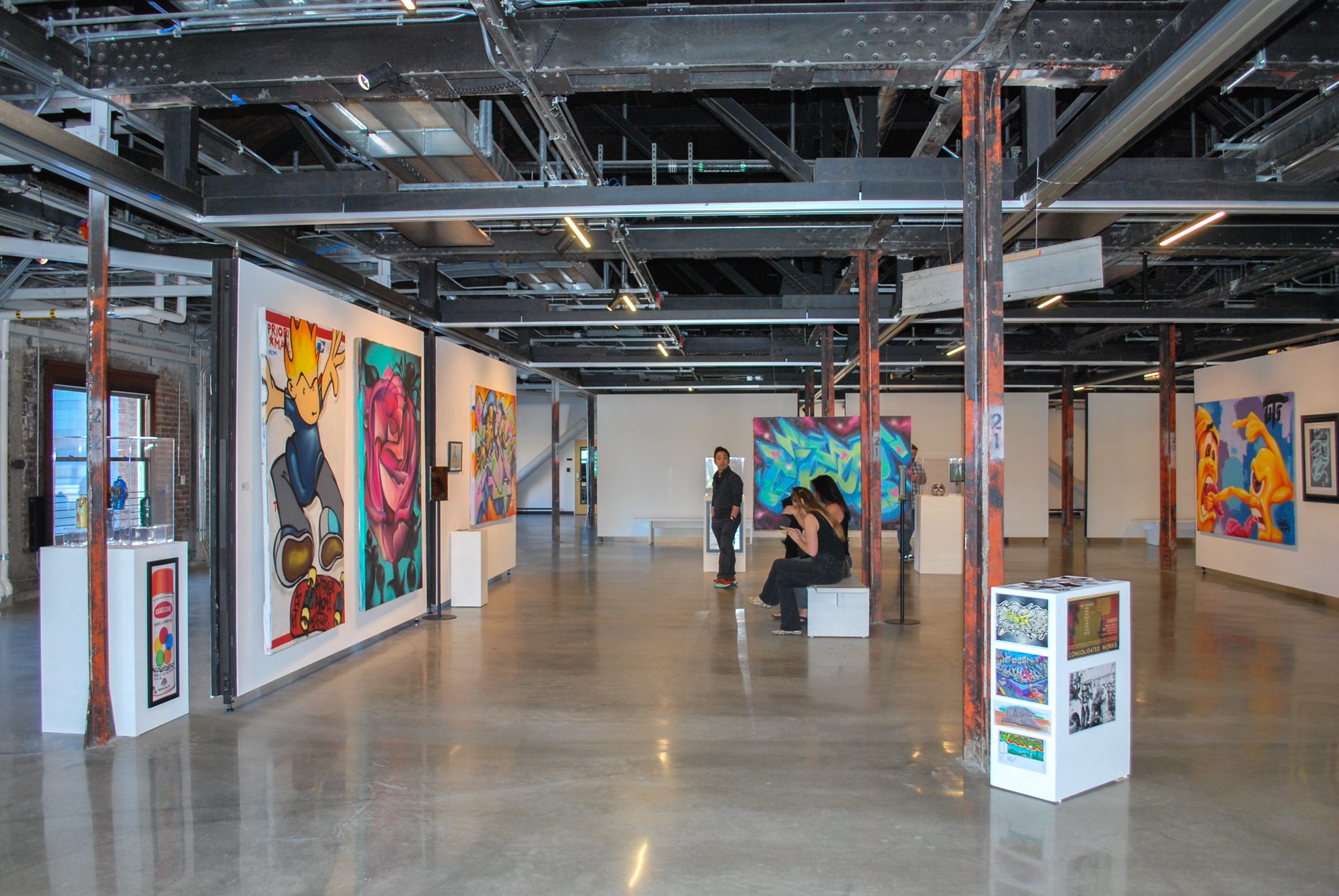 Gallery space filled with graffiti art with three visitors