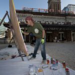 Sire One painting graffiti on canvas in front of King Street Station