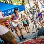 Two Black musicians play guitars outside before a crowd in Pioneer Square