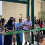 Mayor Bruce Harrell and Kalina Chung smile while they cut a grand opening ribbon in front of Kalina's artwork with comically large scissors.