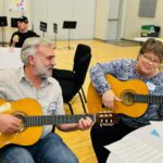 Two people playing guitar in a class setting.