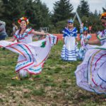 Two Central American women dance joyfully in a park while spinning the skirts of their white dresses