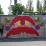 An abstract colorful crying face made with panels of various shapes attached to a fence.