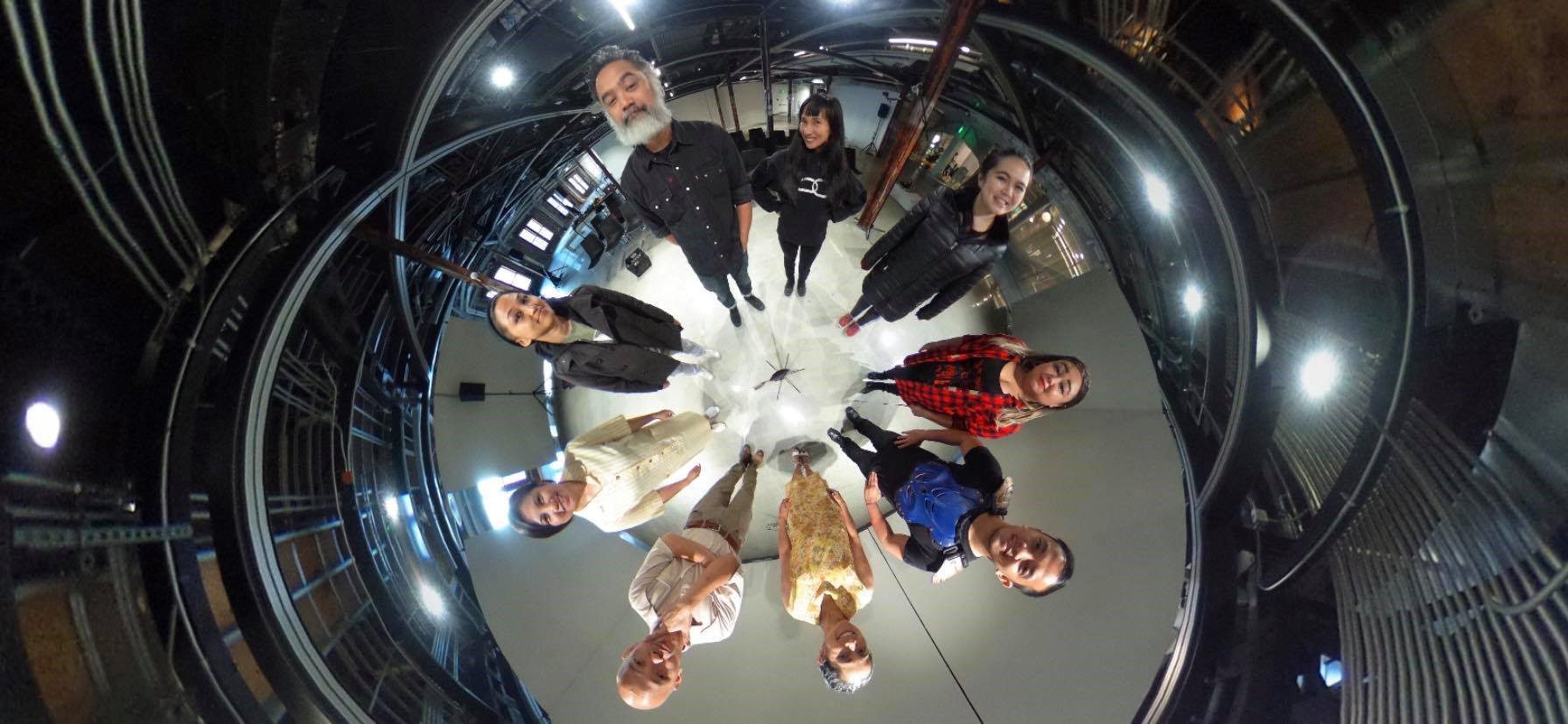 9 people stand in a circle for a 360 degree photo. Their heads appear larger than their bodies.