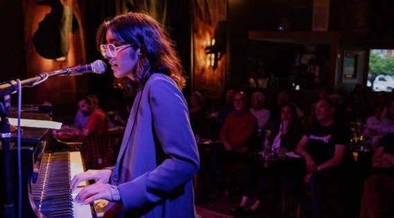 a woman plays piano and sings to an audience.