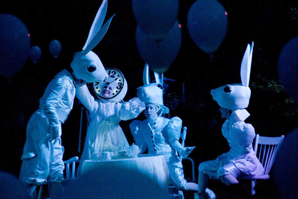 three people dressed as rabbits and one dressed as a clock at a tea party setting