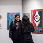 Two women talk in the gallery surrounded by paintings