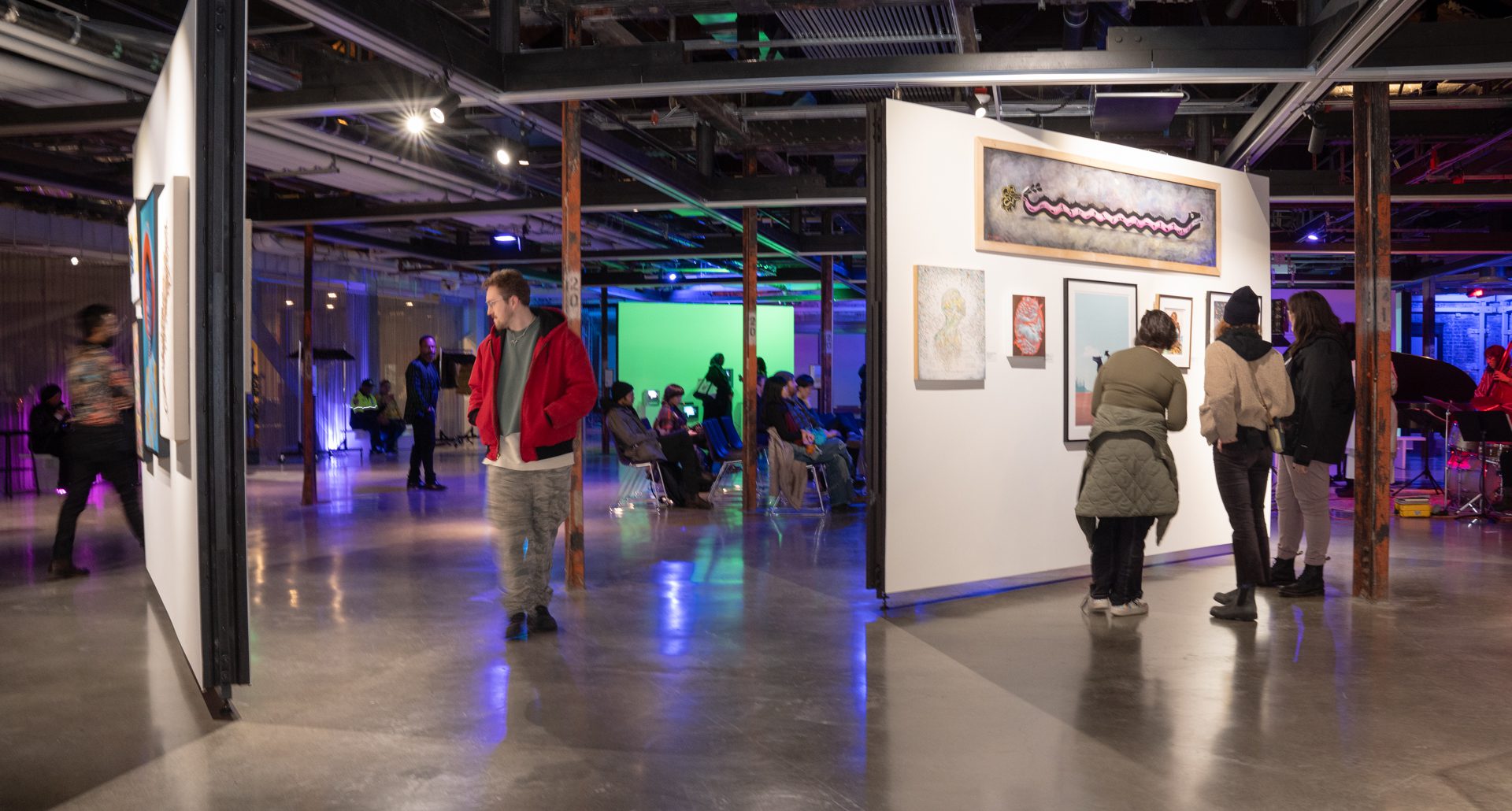 A wide shot of the gallery with people seated in the background and visitors walking around to look at various salon-style art on the walls.