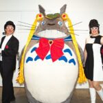 Three cosplayers: two Tuxedo Masks and one large Totoro with Sailor Moon braids and accessories. It's hilarious.