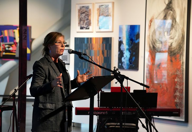 Gülgün at the mic, art hanging on the gallery walls behind.