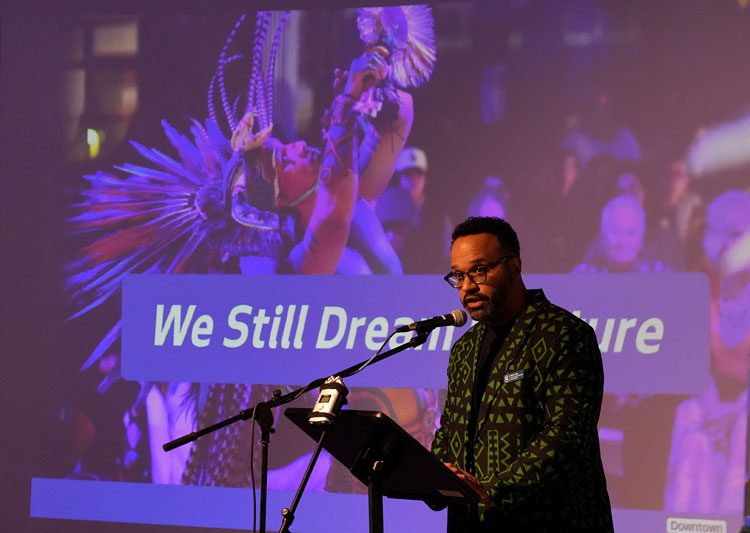 James speaks in front of a slide that says We Still Dream a Future