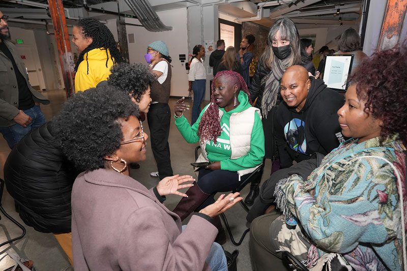 A group of Black guests sit in a circle talking