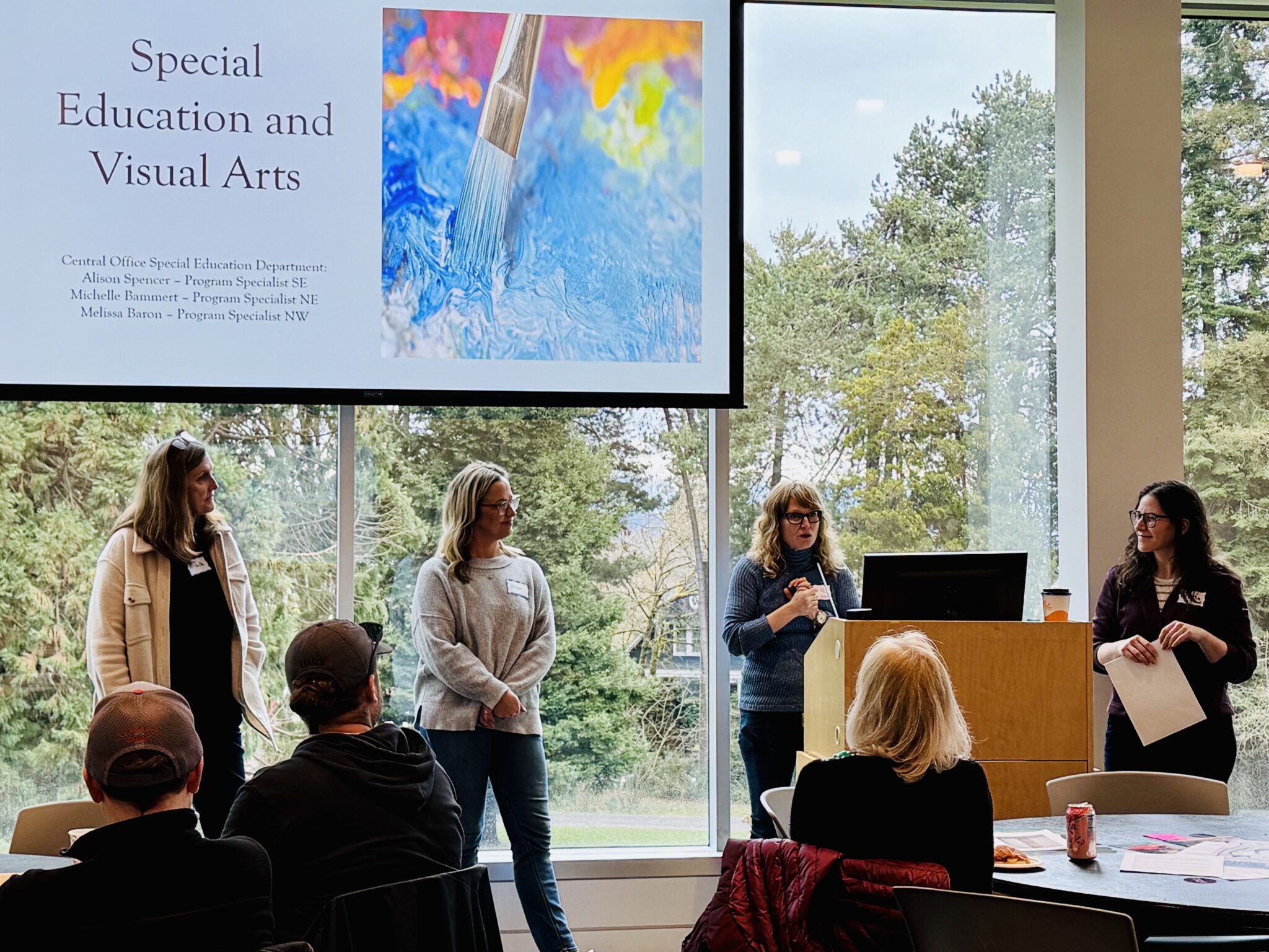 four women stand and present, reading a slide that says 