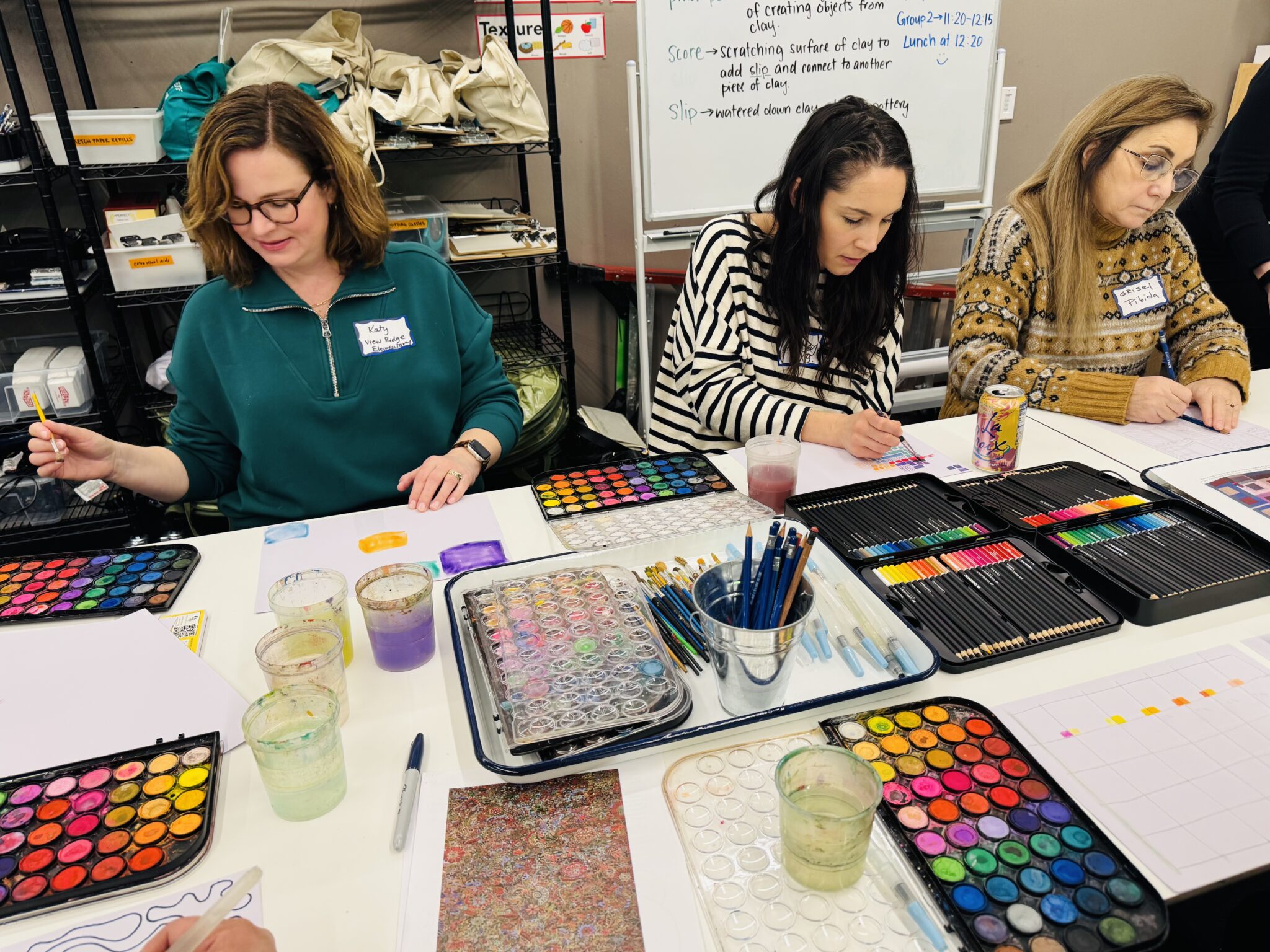 Three teachers sit at a table and paint with watercolors