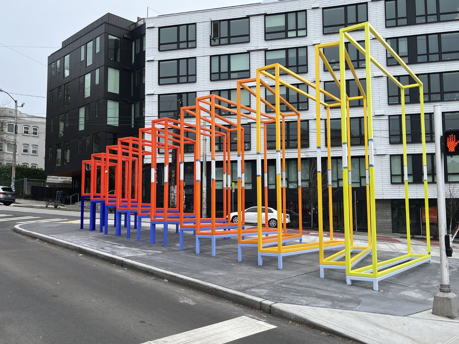 ombre yellow to red large hallow square structures that go small to large installed on a sidewalk