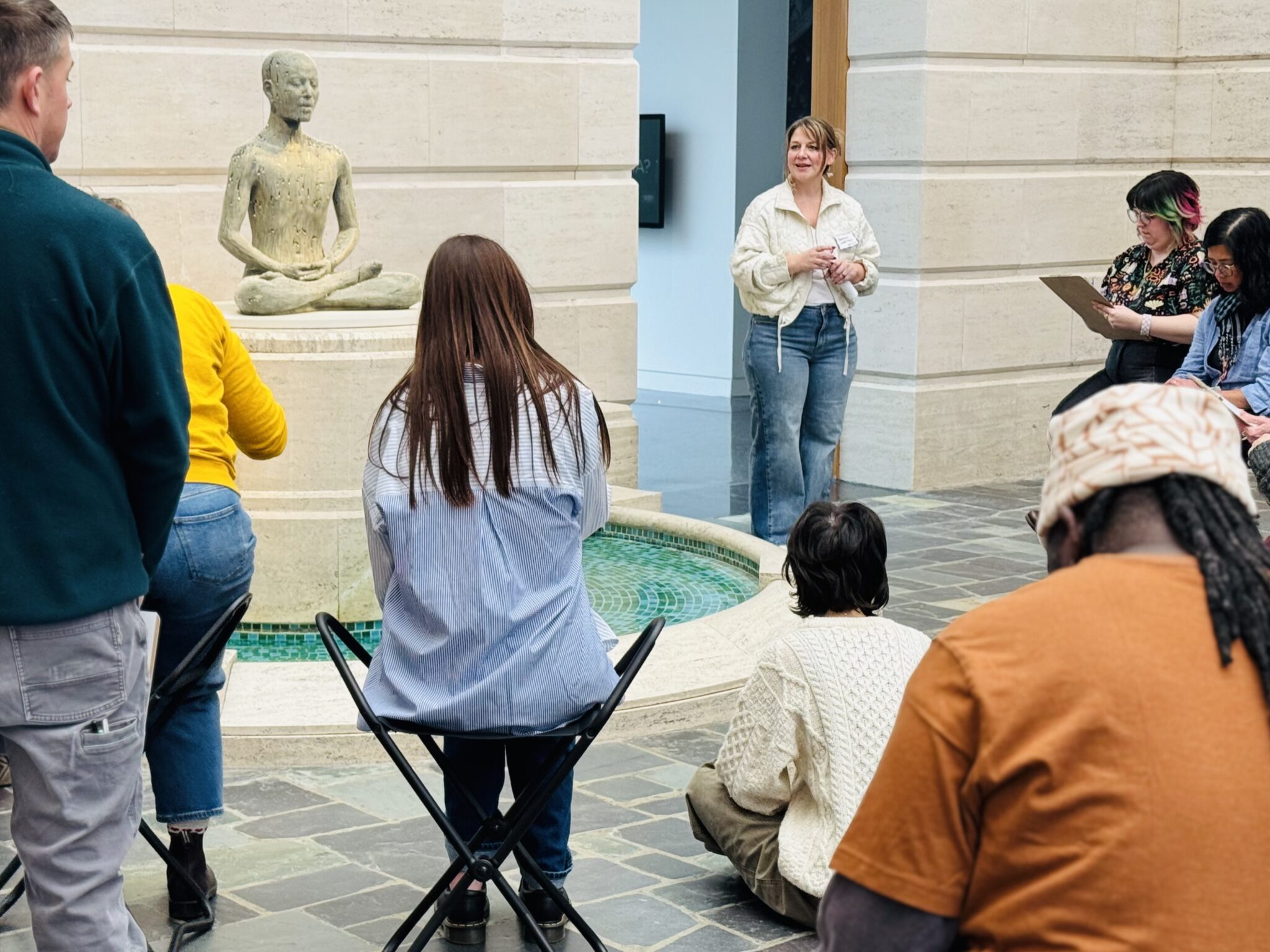 A woman stands and speaks to a seated audience in the Seattle Asian Art Museum