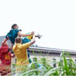 Two dancers in colorful jumpsuits hold a third up to the sky.