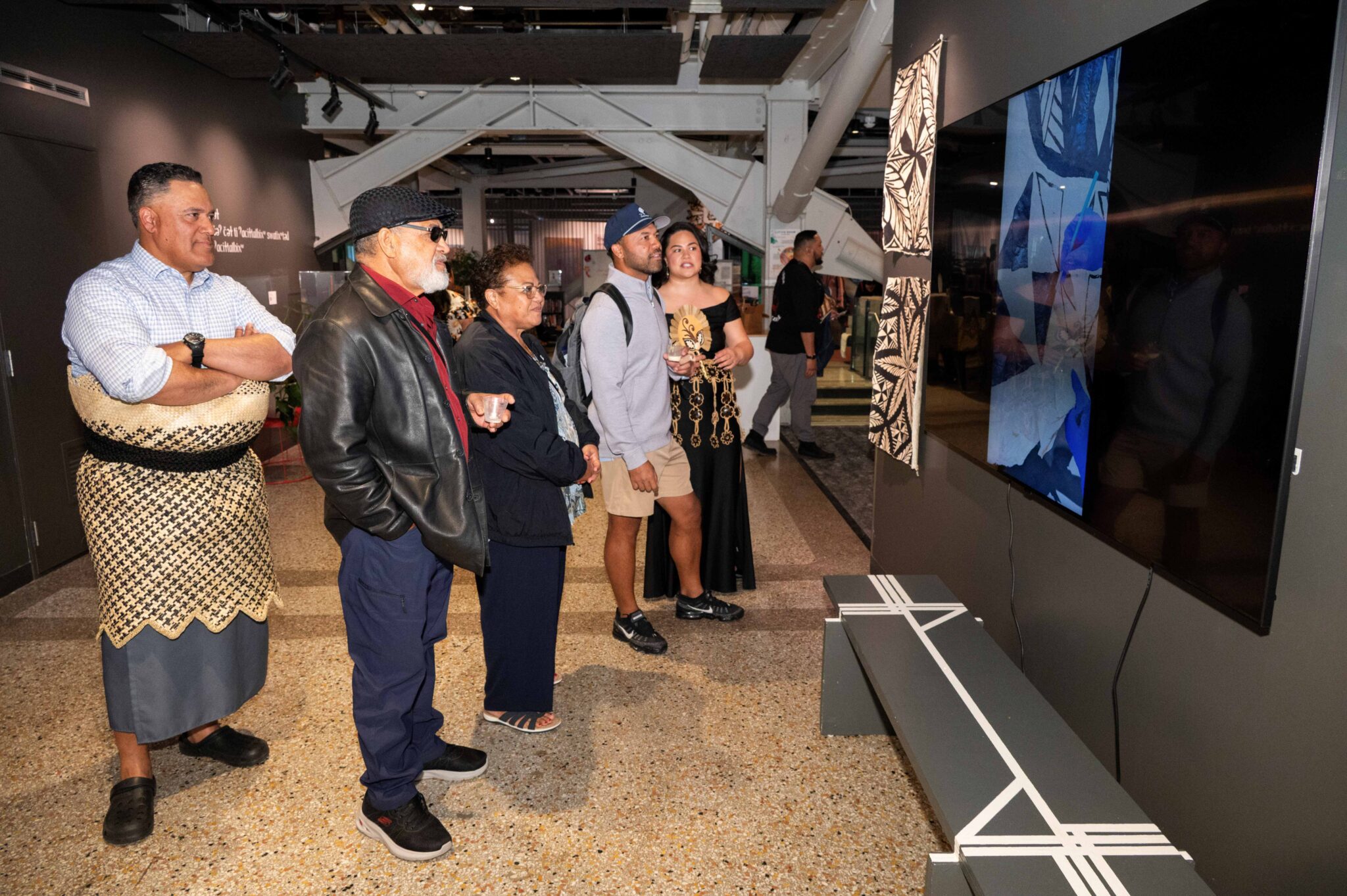five people stand and watch art on television