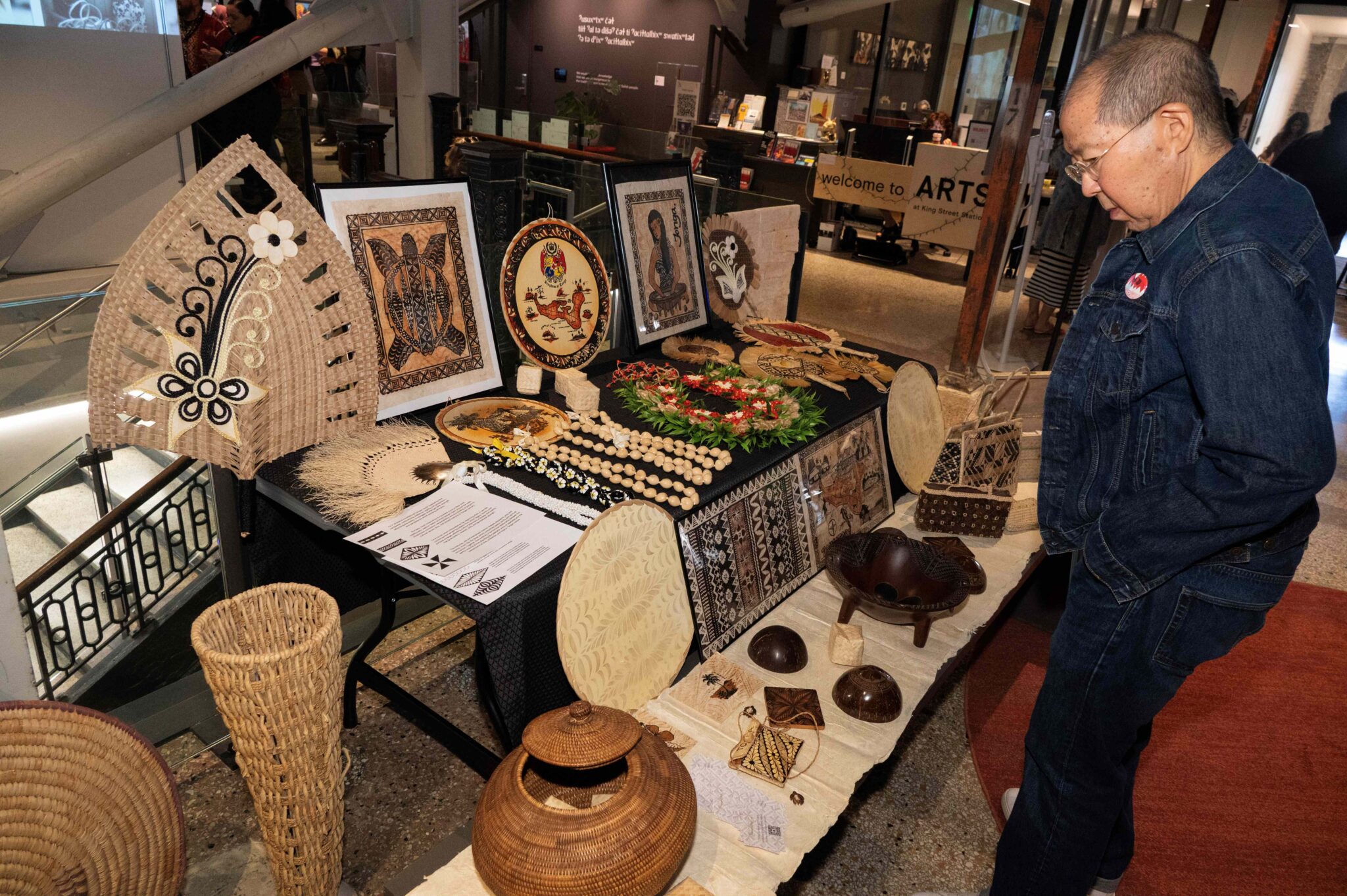 A man looks at a table of Tongan weaved baskets, picture, and jewelry