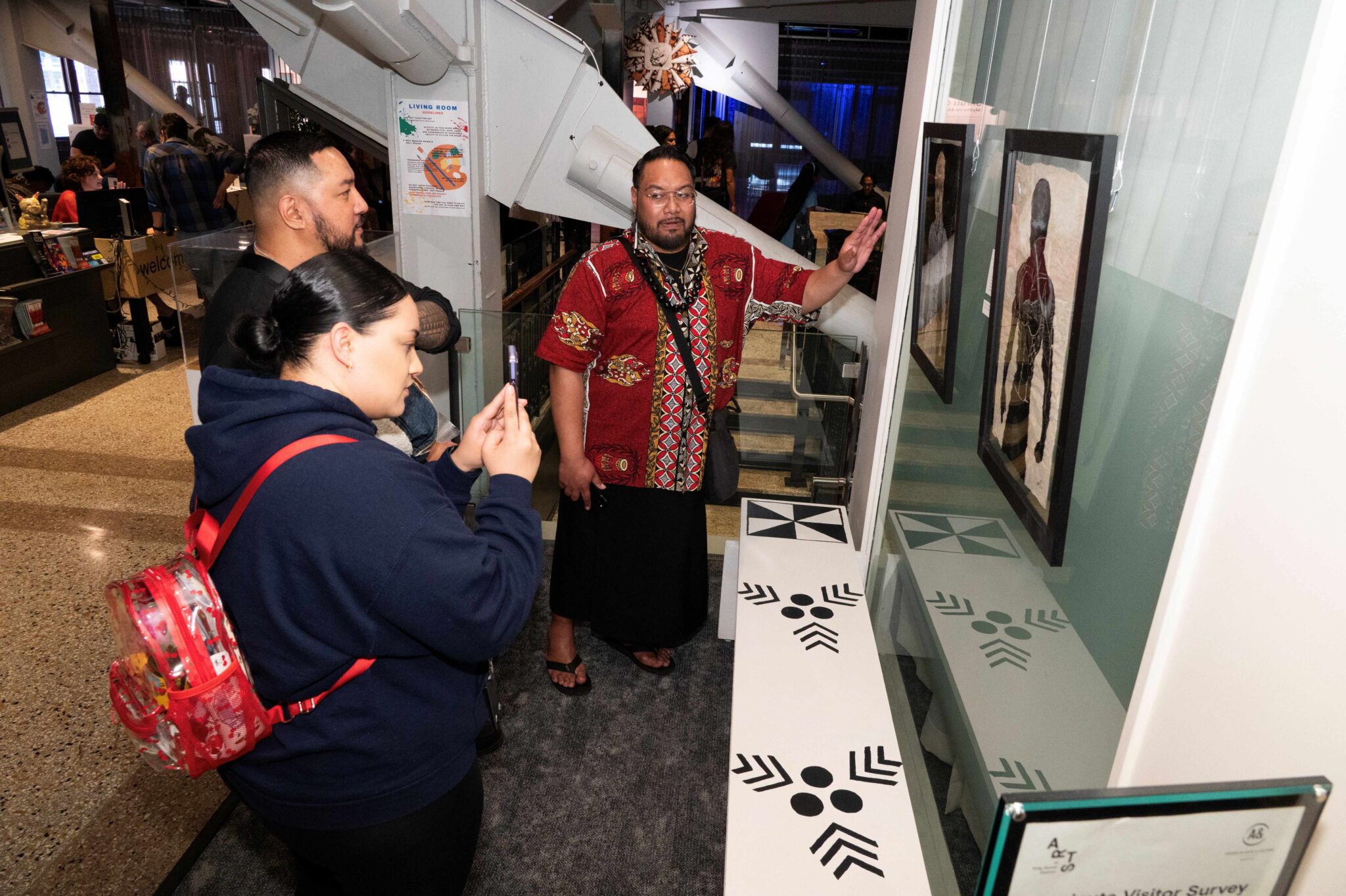 A man gestures towards a painting while a woman takes a photo on her phone