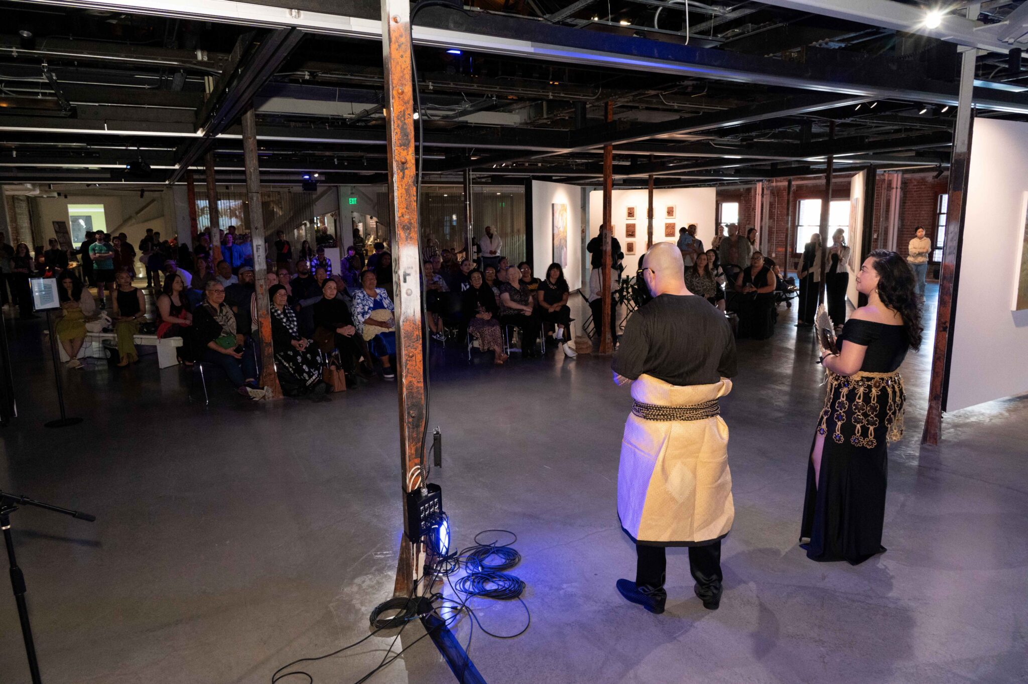 Two people speak to a large crowd in the gallery