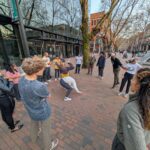 two people breakdance in pioneer square with a group watching around them