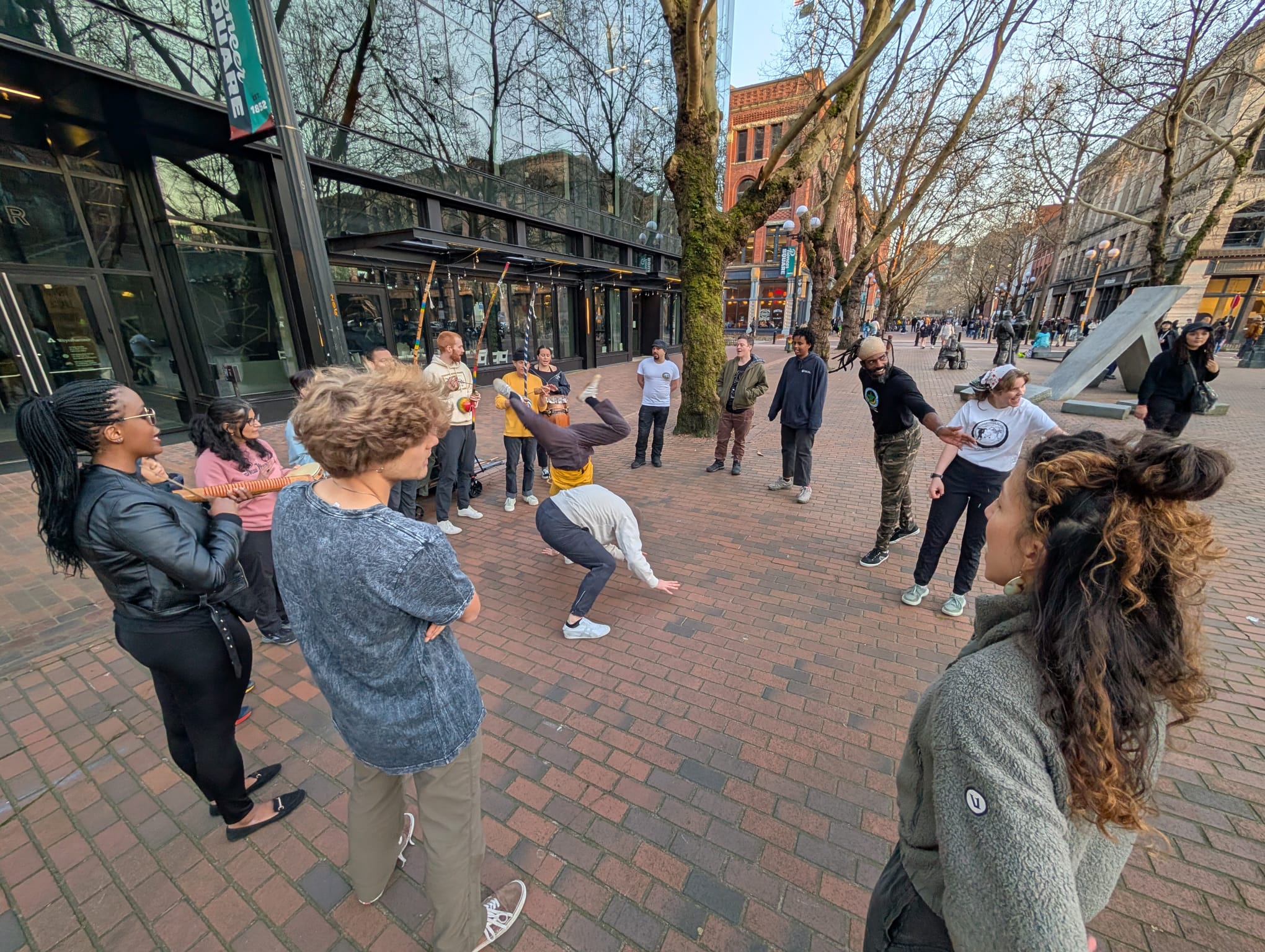 two people breakdance in pioneer square with a group watching around them