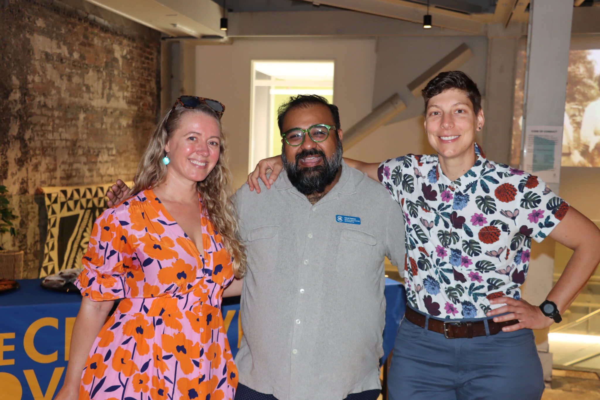 Three people smile and look at the camera with their arms around each other's shoulders.