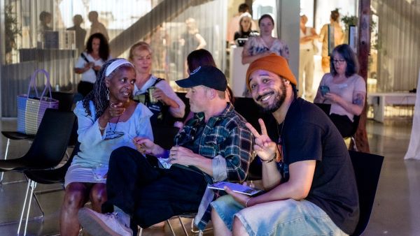 Bearded person in orange beanie smiles at camera while chucking up their deuces.
