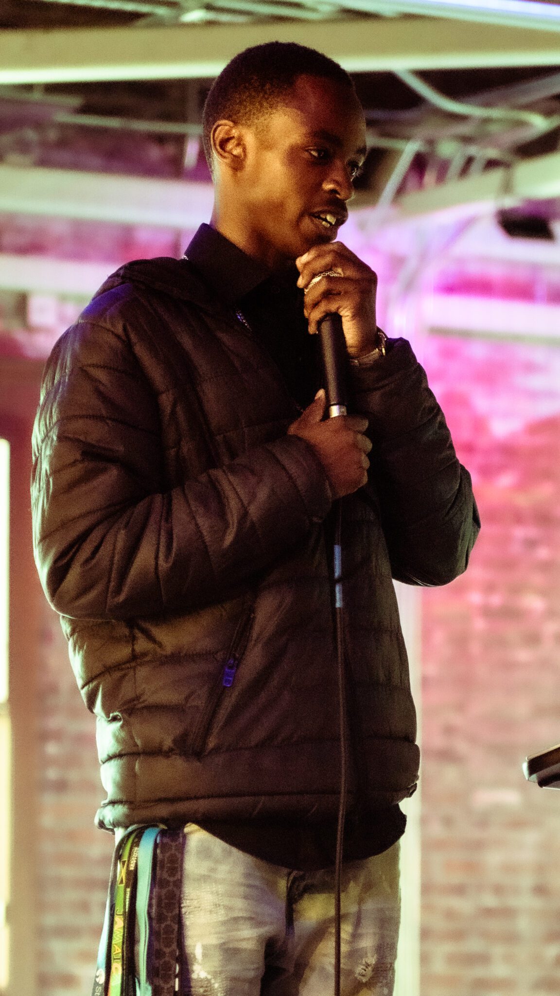 A teen with a buzz cut in a puffer jacket holds a microphone.
