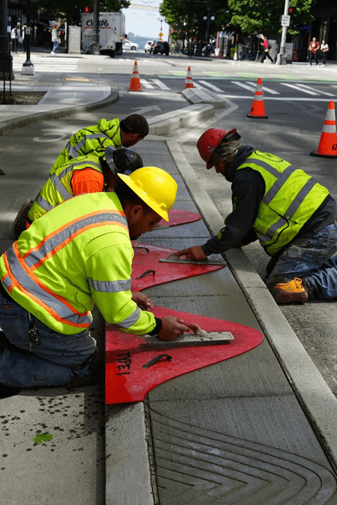 Four construction workers stamp designs into concrete bike buffers on a Seattle street.