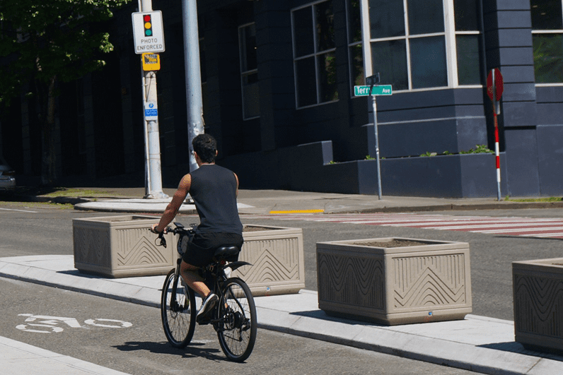 Person bikes past concrete planters feature the wave design in relief in a Seattle bike lane.