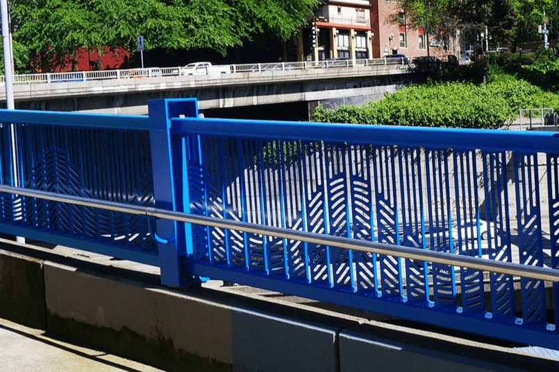 A close-up image of a bright blue custom railing on the Pike and Pine overpasses over I-5 that features a wave pattern.
