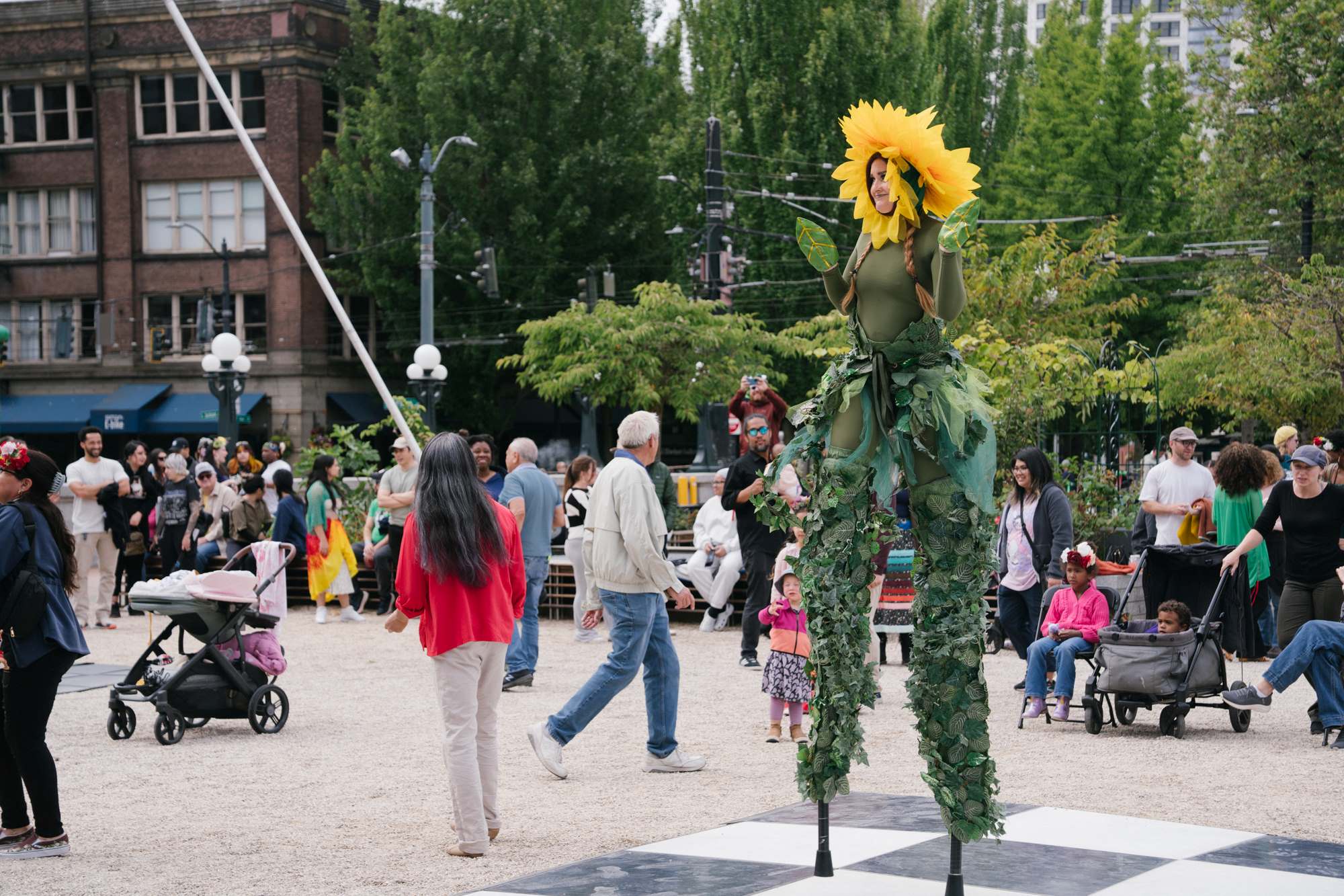 A woman on stilts and dressed as a sunflower walks around on the King Street Station plaza dance floor