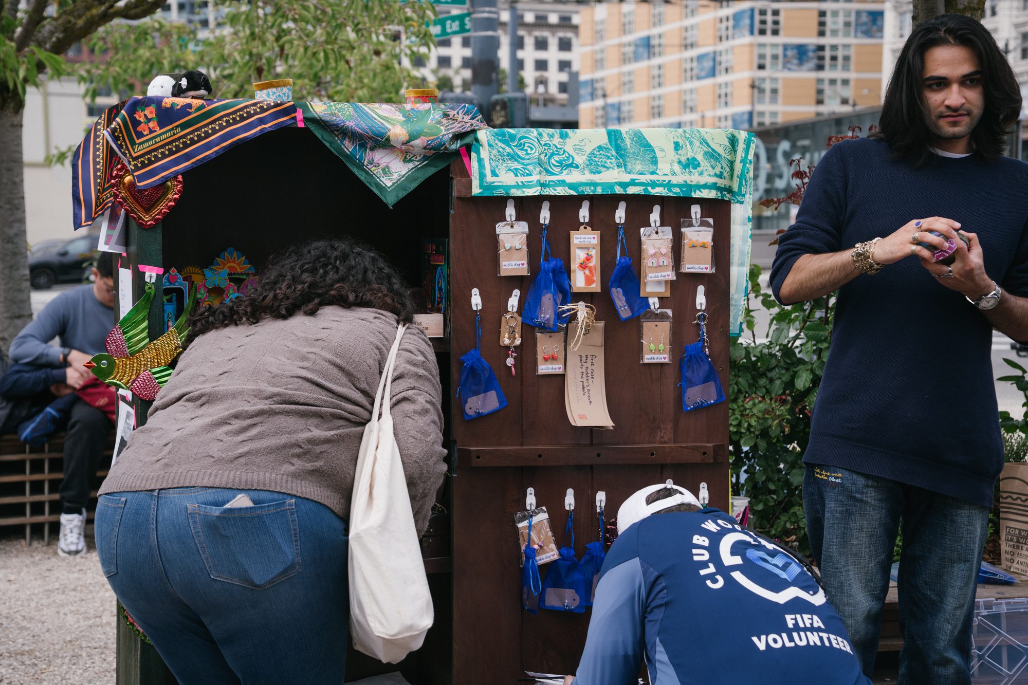 People kneel next to cabinet with an open door that is laden with gifts of free art.