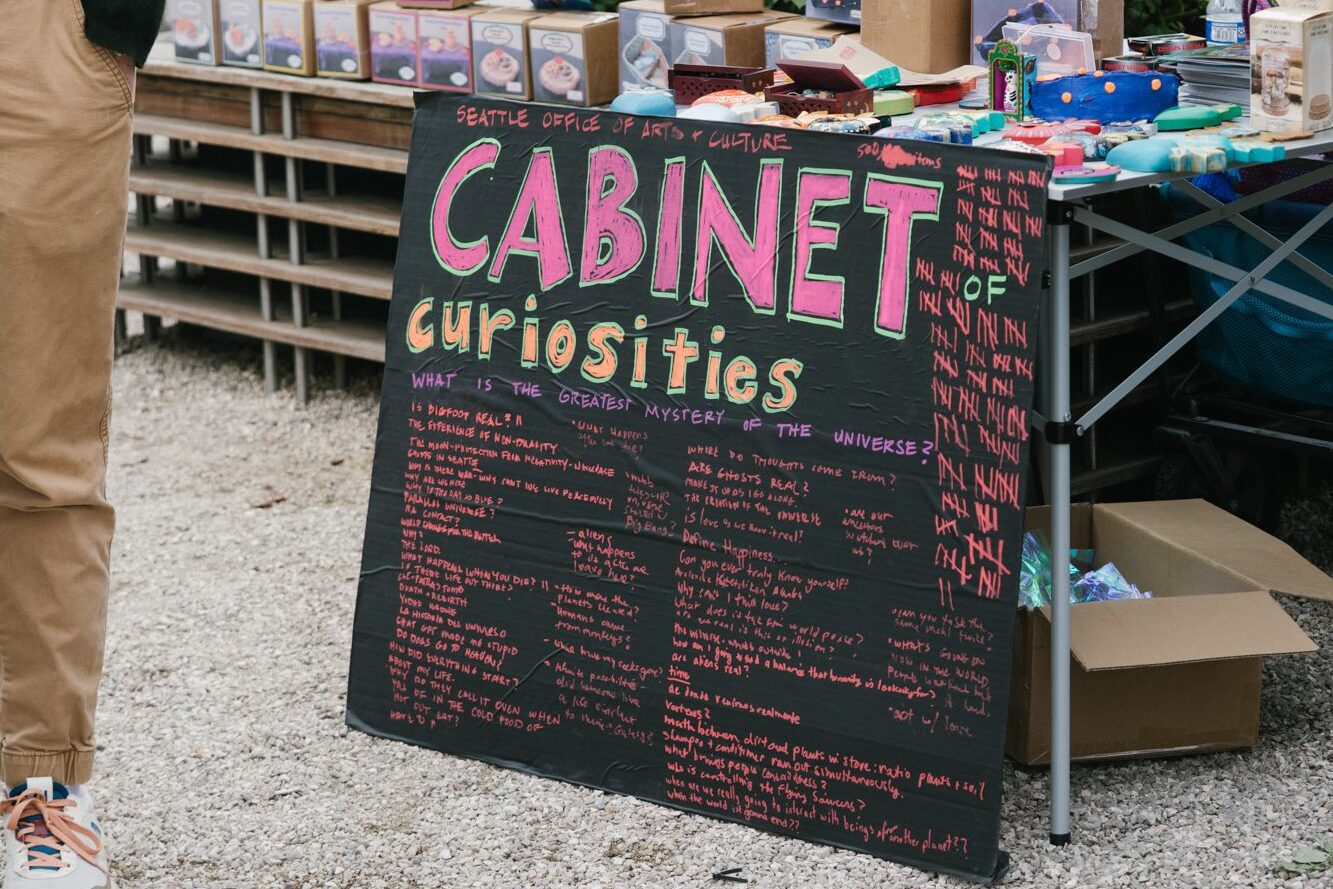 A photo of a sign that reads " Cabinet of Curiosities, what is the greatest mystery of the universe?"