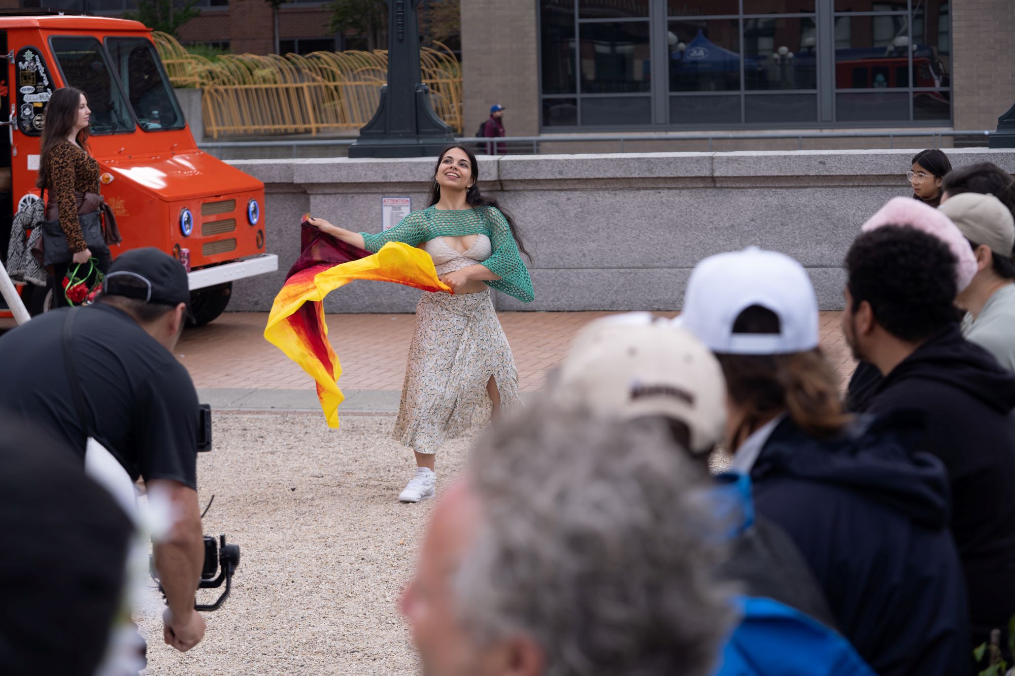 A woman waves a colorful fabric around with an audience watching