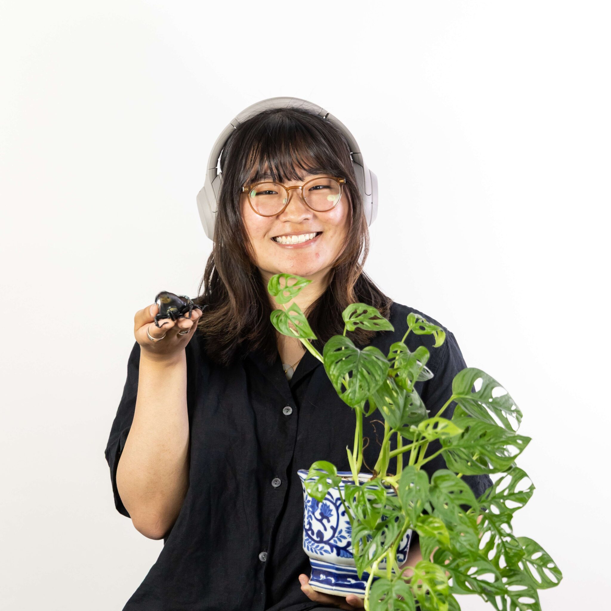 Vivian wears headphones and hold a potted plant and a small frog