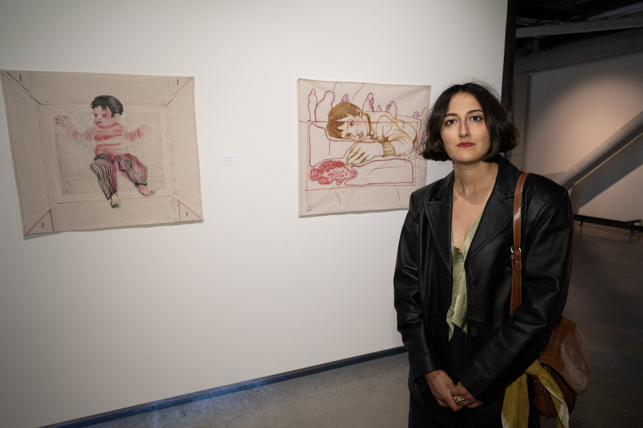 A femme person with a bob and lipstick poses in front of two multimedia artworks.