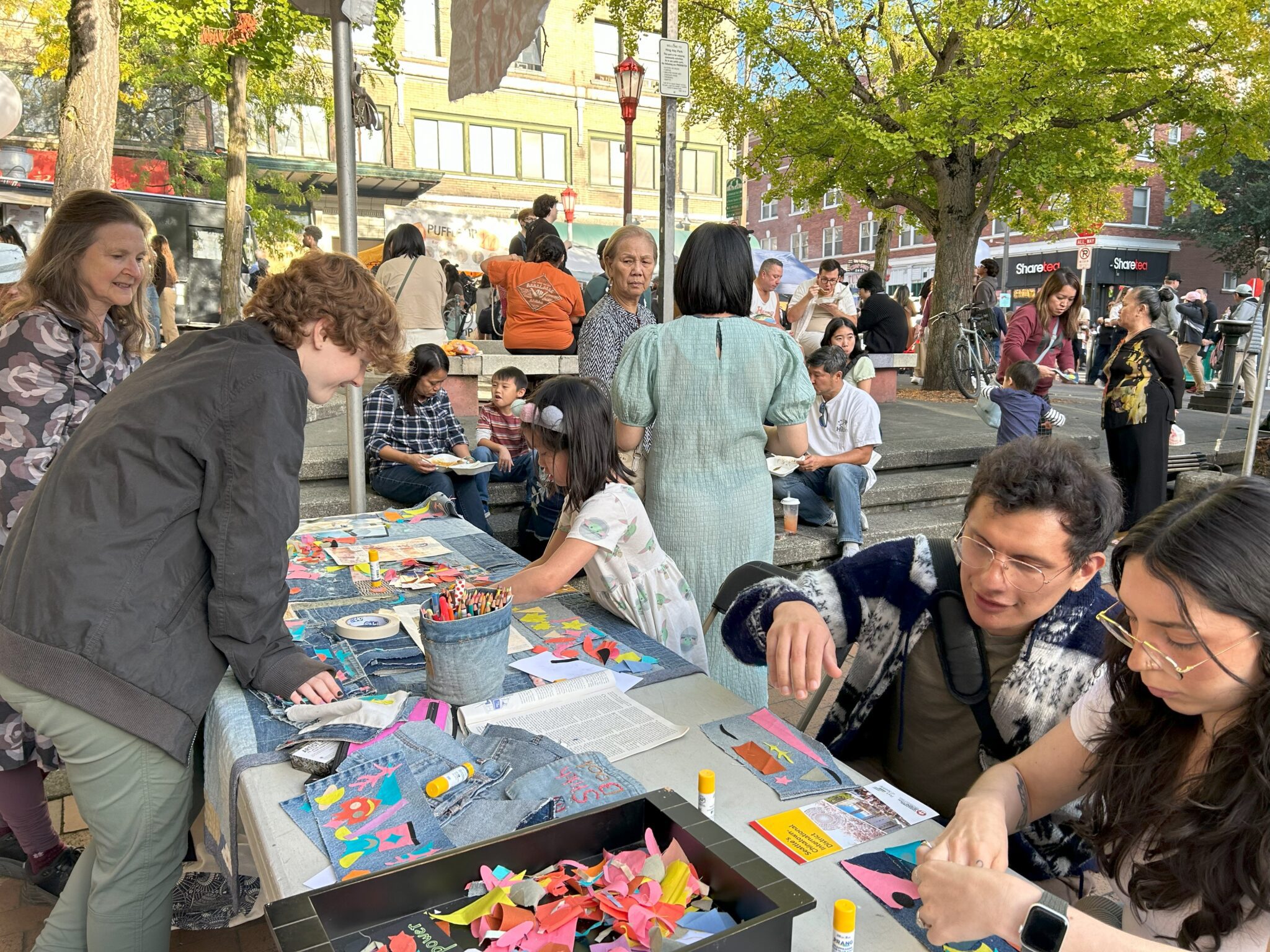 People work on collages outdoors at a table filled with textile scraps.