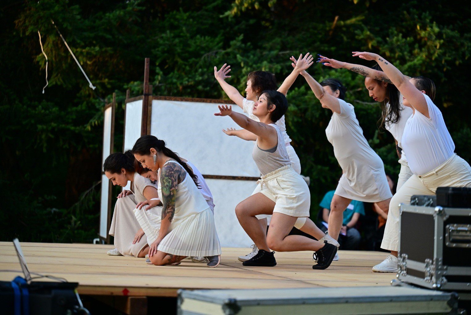 Six figures in white dance on an outdoor stage.
