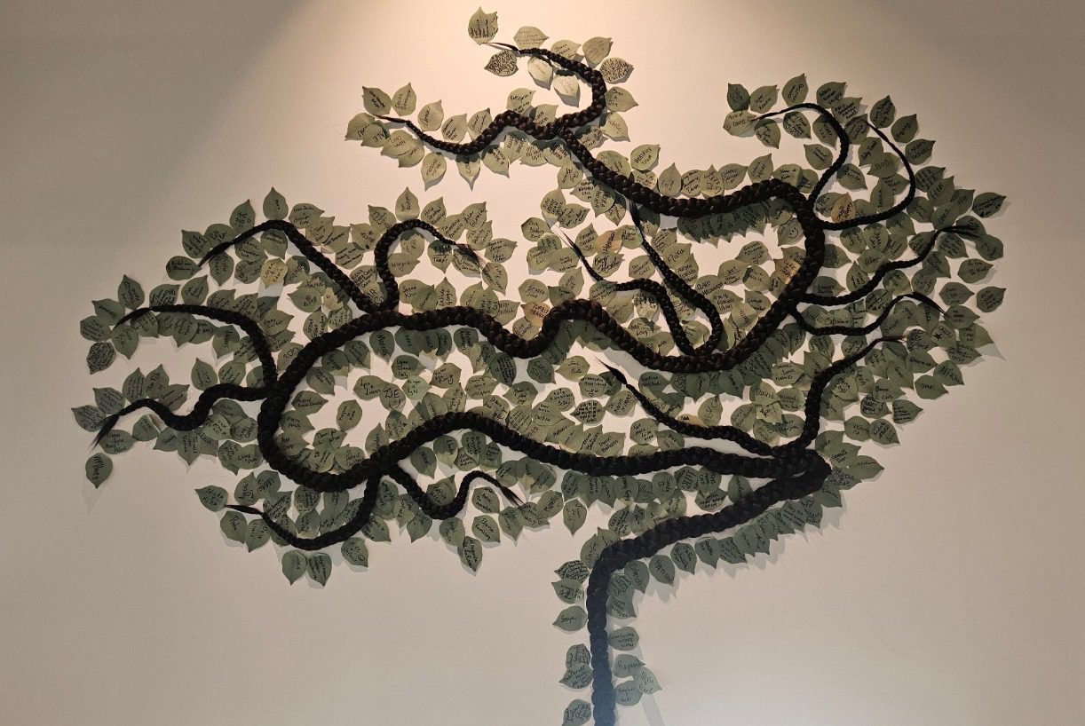 A tree-like flat sculpture on the wall with green leaves attached