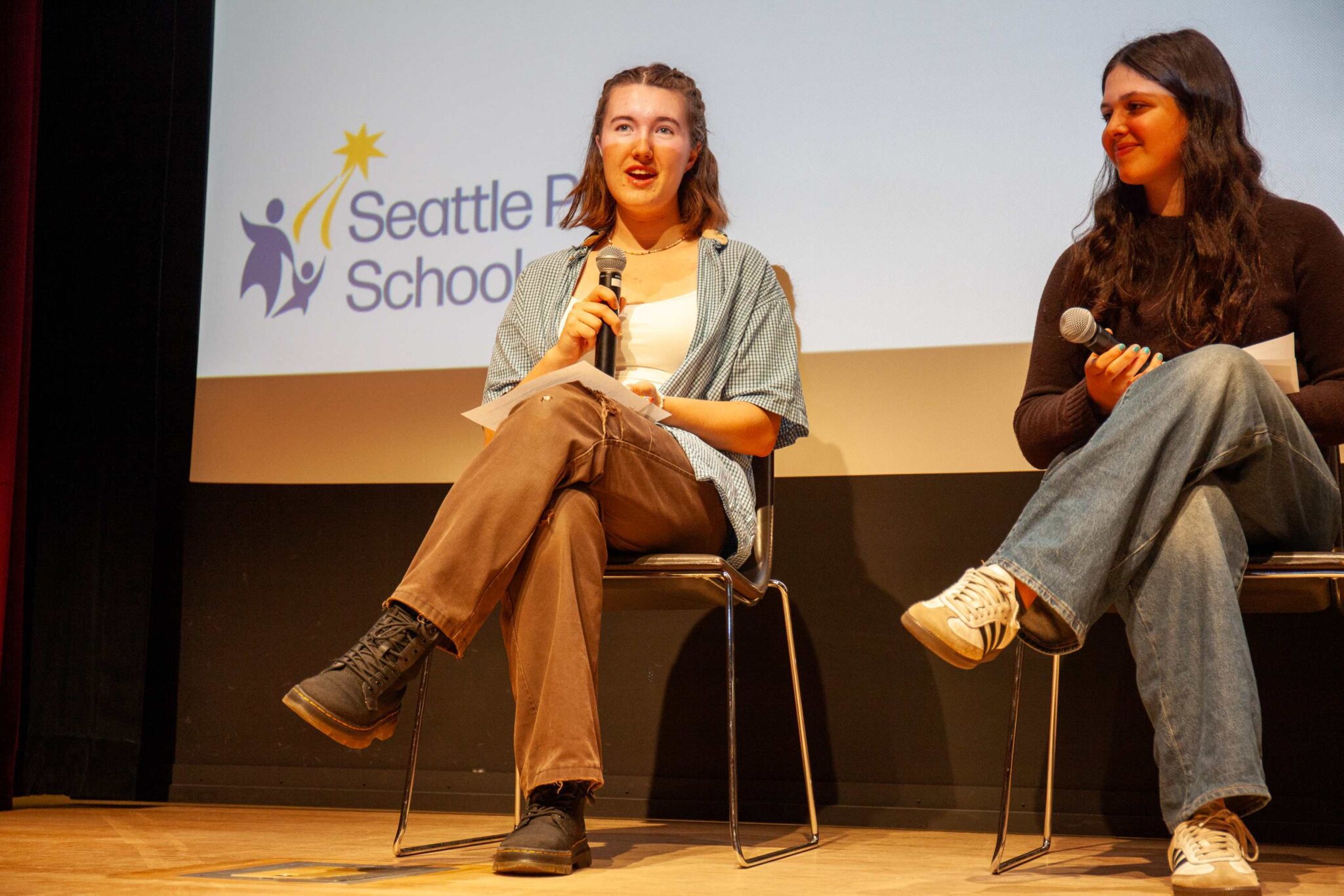 A student sits in chair and speaks into a mic on stage